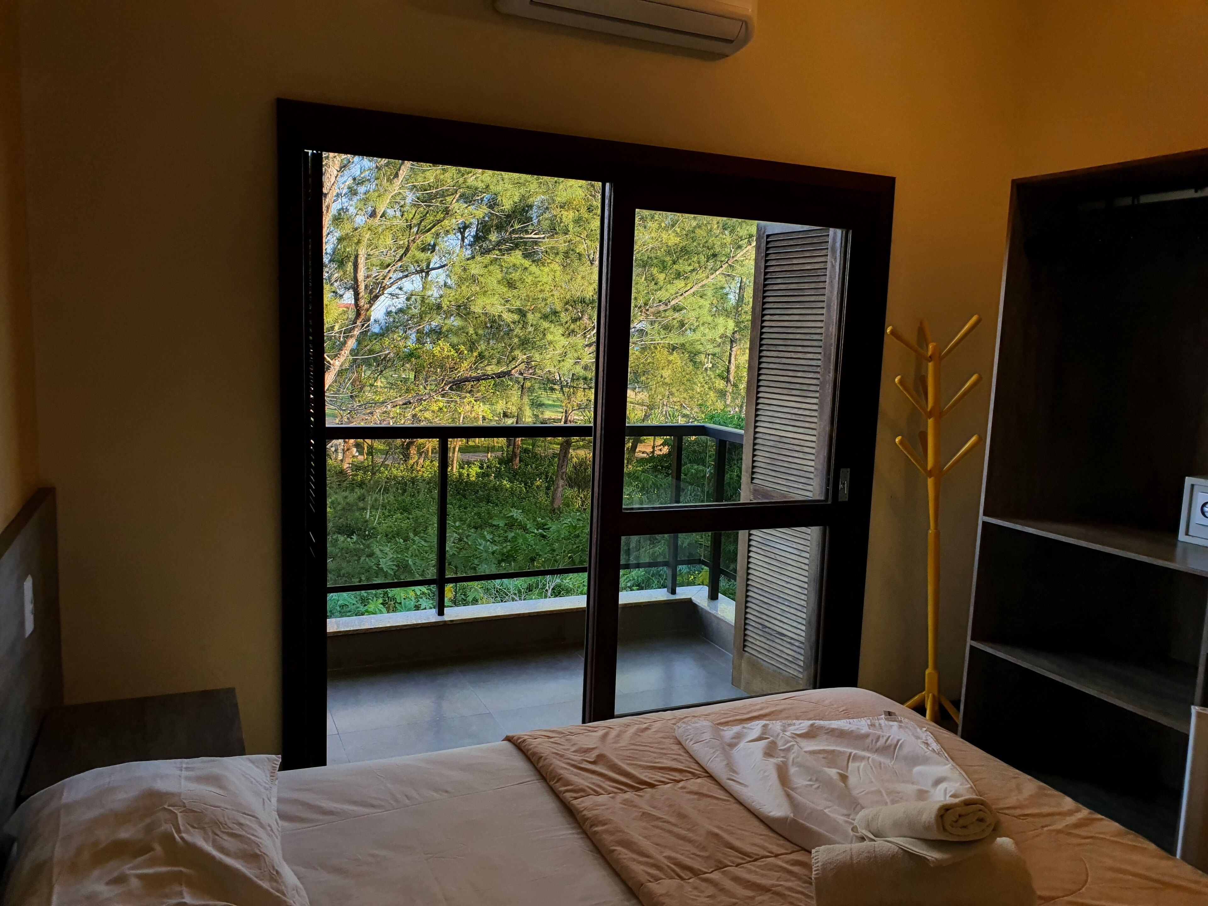 A bedroom with a bed, a window with a view of greenery, and a shelf with a towel.