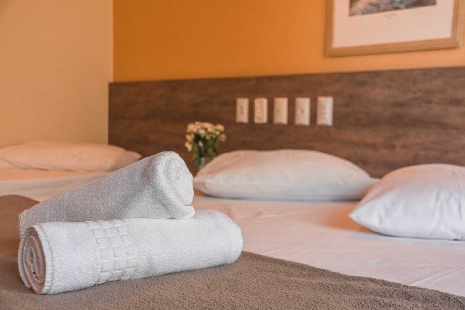 A neatly made bed with white pillows and a rolled white towel on a brown bedspread.