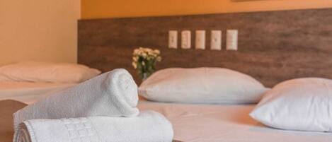 A neatly made bed with white pillows and a rolled white towel on a brown bedspread.