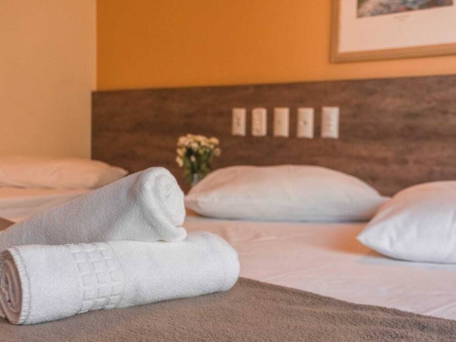 Een net opgemaakt bed met witte kussens en een opgerolde witte handdoek op een bruine deken.