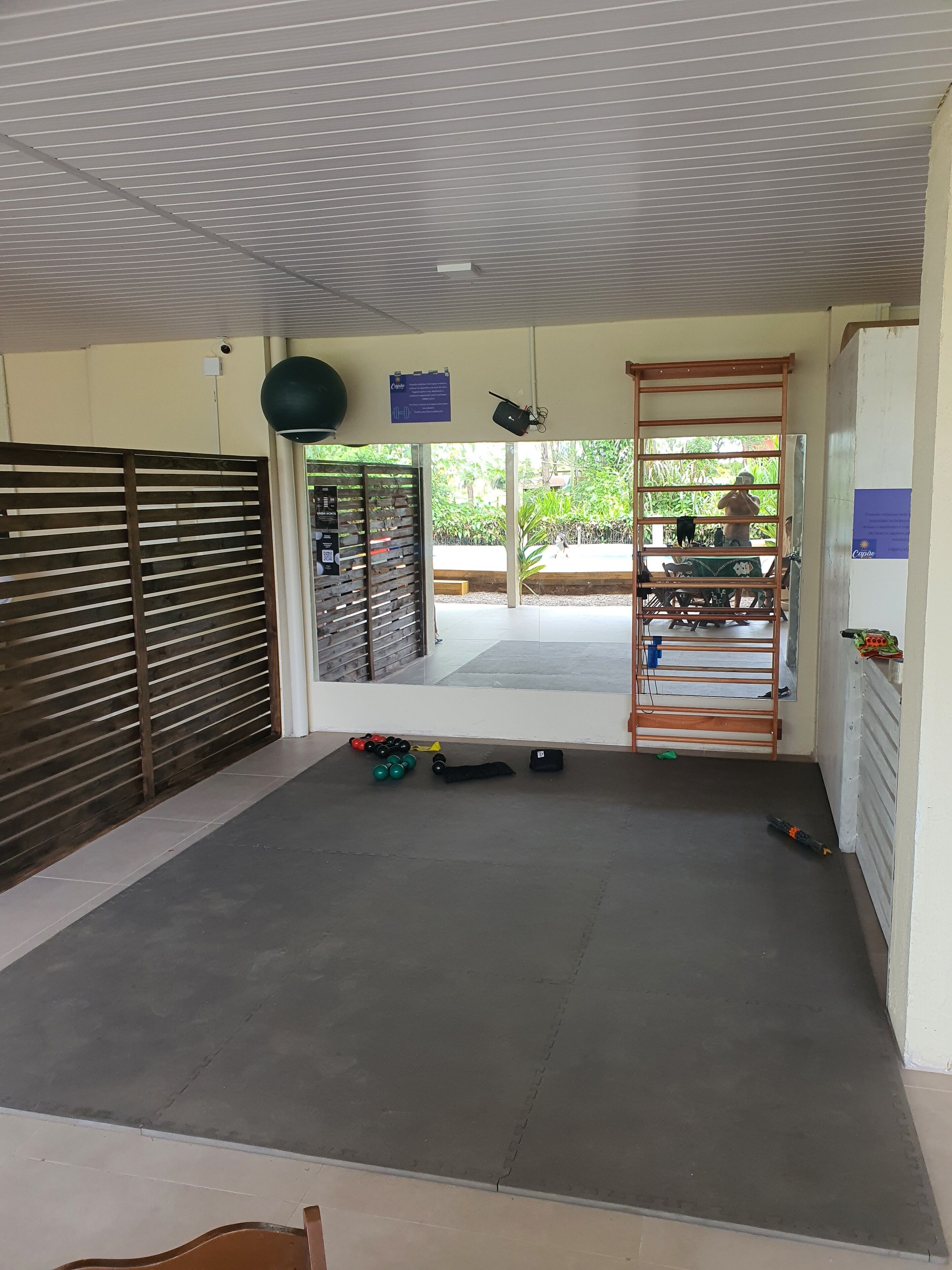 Espaçoso espaço interno com piso de concreto, divisória de madeira e portão de metal que dá para o exterior.