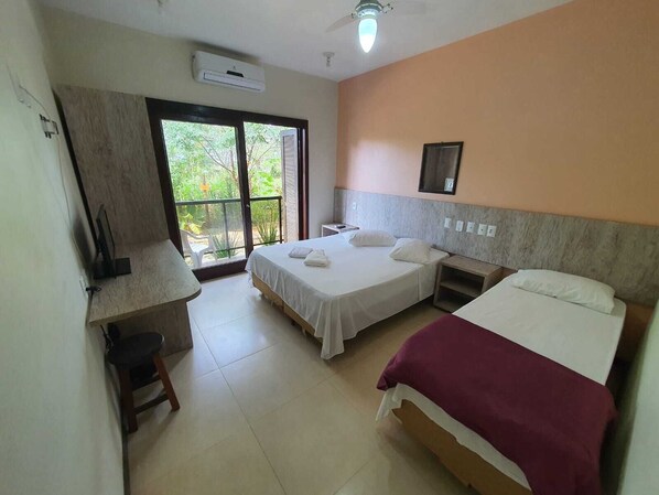 A hotel room with two beds, a desk, a chair, and a large window with a view of greenery. - Hotel Pousada Capão (Garopaba)