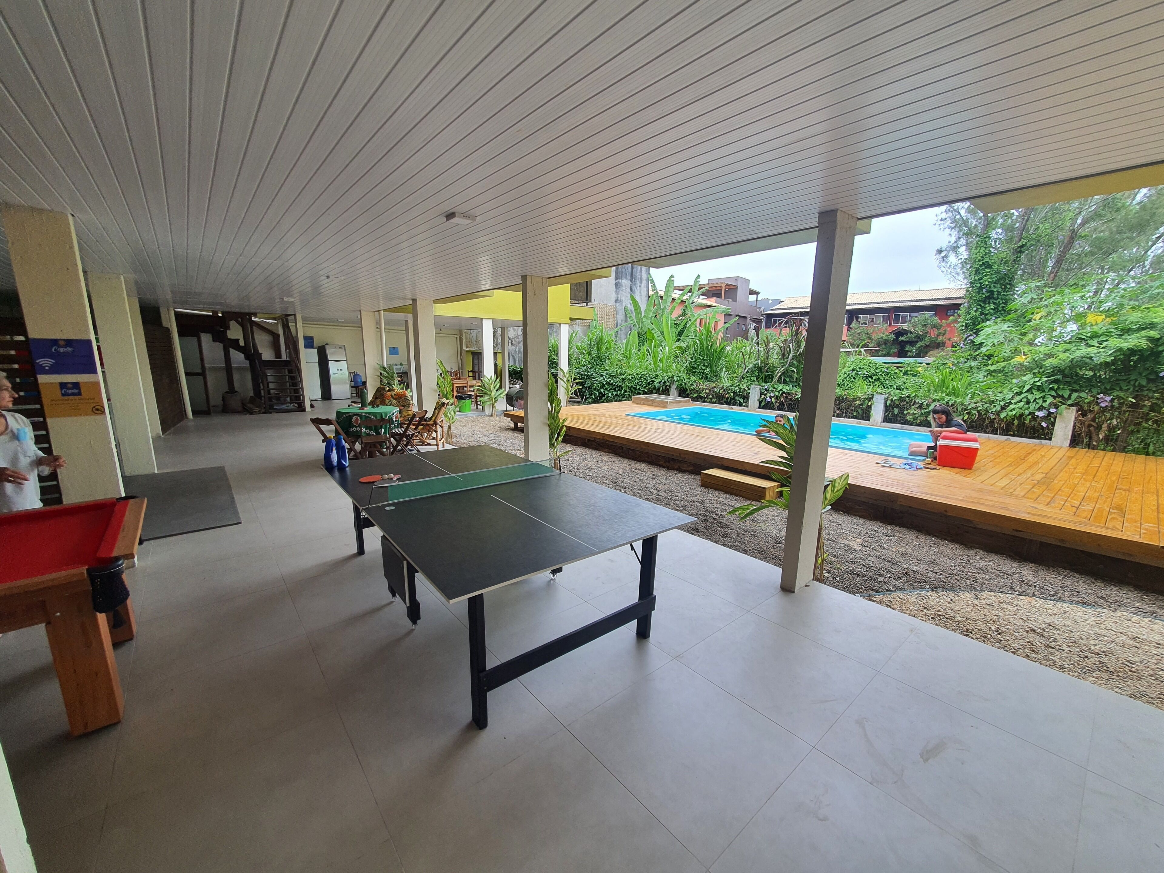 Uma área externa coberta com mesa de pingue-pongue, piscina e área de refeições com cadeiras e mesas.