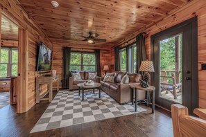 A log cabin interior with a checkered rug, leather sofa, and a ceiling fan. - Elevate your Smoky Mountain Stay - Upscale Decor & Unforgettable Mountain View! (Sevierville)