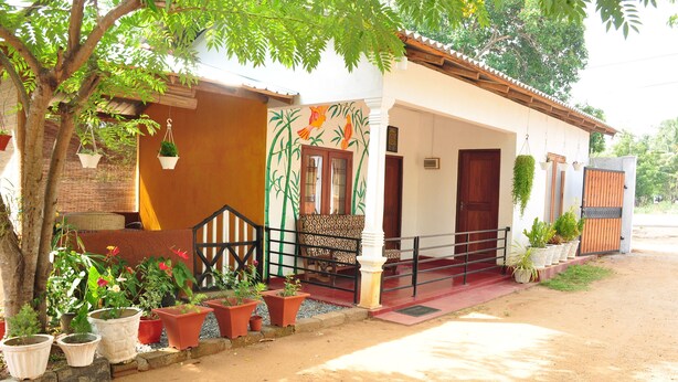 A house with a porch, potted plants, and a staircase leading to the entrance. - Pawansa Homestay (Habarana)