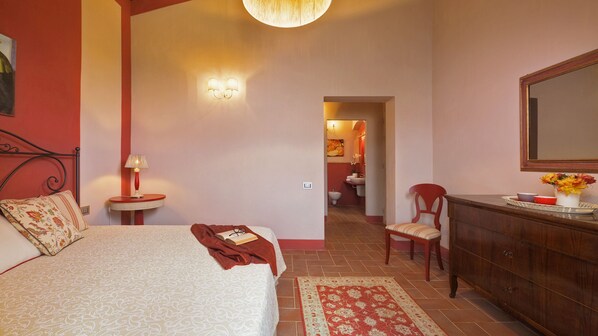A bedroom with a bed, bedside tables, a dresser, a chair, and a bathroom visible through an open door. - Villa il Magnifico 10, Emma Villas (Reggello)