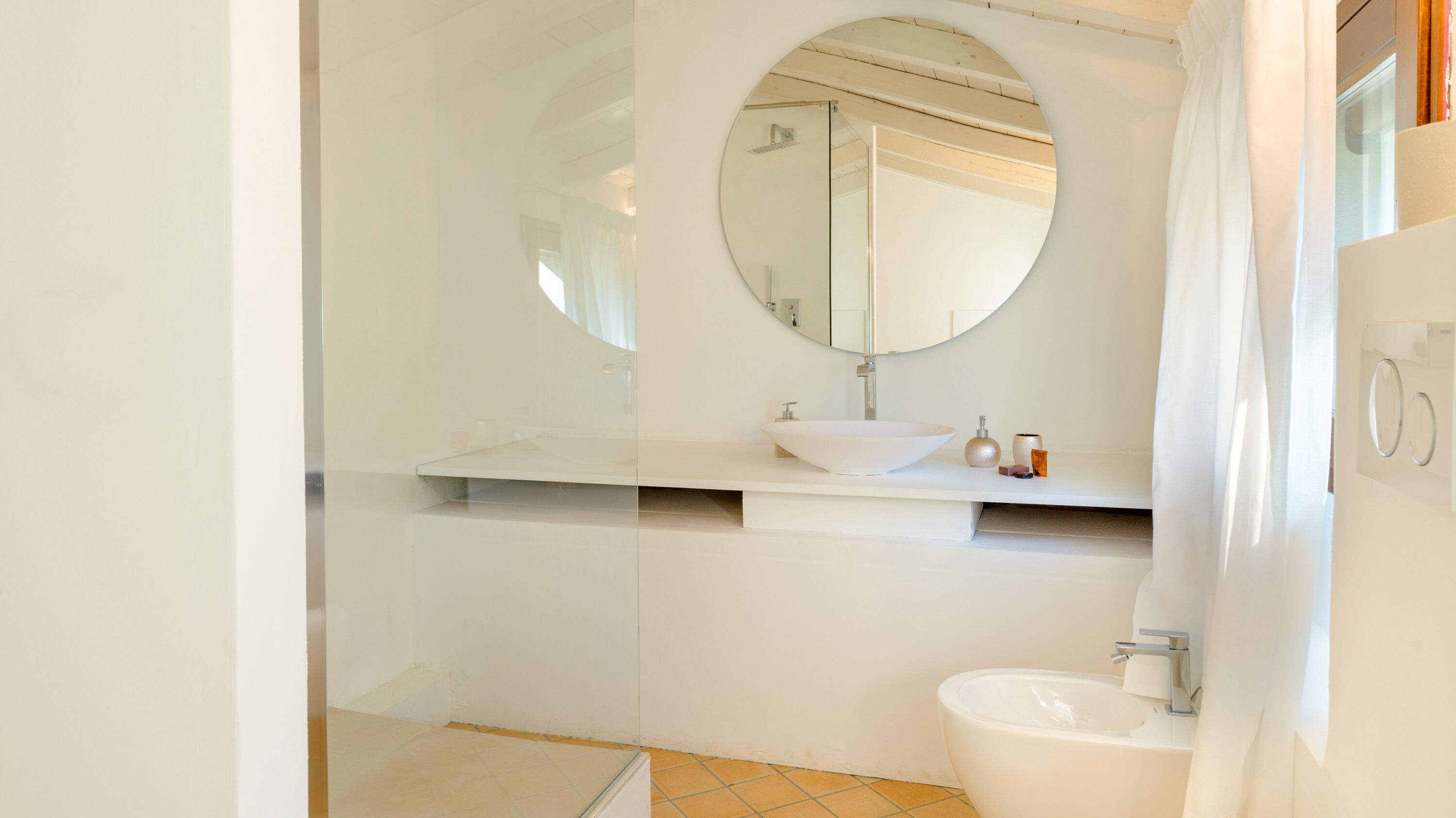 A modern bathroom with a white sink, a round mirror, and a toilet.