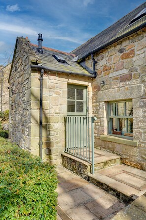 A stone building with a small entrance, a window with a nameplate, and a chimney.