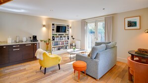 A modern living room with a sofa, ottoman, and yellow chair. There is a kitchen area with cabinets and a dining table. - South Stable: Cosy Stone Retreat with Parking (Alnmouth)