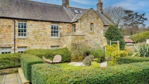 A stone building with a garden, a staircase, and two chairs. - Pope Lodge: Cosy Stone Coach House in Alnmouth (Alnmouth)