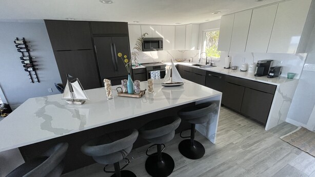 A modern kitchen with a large island, dark cabinetry, and a window providing natural light. - Beachfront House with Beautiful Ocean Views and Private Beach Access (Melbourne Beach)