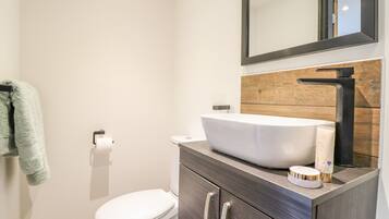 A modern bathroom with a white toilet, a large white sink, and a wooden vanity.