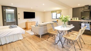 A modern hotel room with a bed, a sofa, a dining table with chairs, a TV, and a kitchen area. - The Cabin at Evelyns Retreat (Corwen)