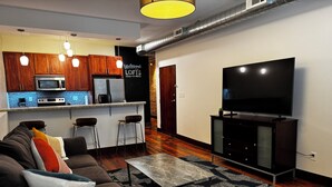 A modern living room with a sofa, coffee table, and a TV. There's a kitchen area with wooden cabinets and a microwave. - Stylish 2BR Loft in the heart of Downtown Paducah (Paducah)