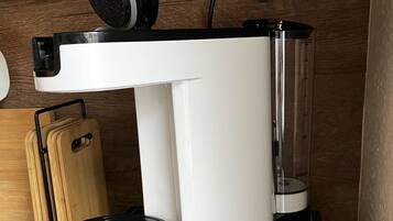 Een compact koffiezetapparaat op een houten aanrecht met een lade eronder.