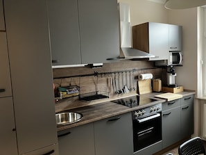 A modern kitchen with grey cabinets, a wooden countertop, a stainless steel sink, and a coffee machine.