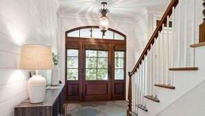 A wooden staircase with a white railing, a wooden door with glass panels, and a lamp on a console table.