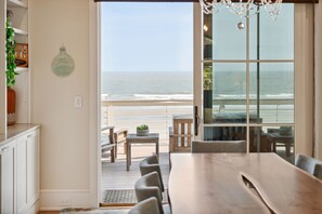 Enjoy a spacious open-plan area with a dining table, chandelier, and glass door leading to a deck with ocean views.