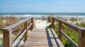 A wooden boardwalk leading to a beach with a clear view of the ocean.