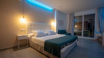 Quarto de hotel moderno com uma cama grande, uma mesa de cabeceira, um tapete verde e vista para o exterior através de uma porta de vidro deslizante.