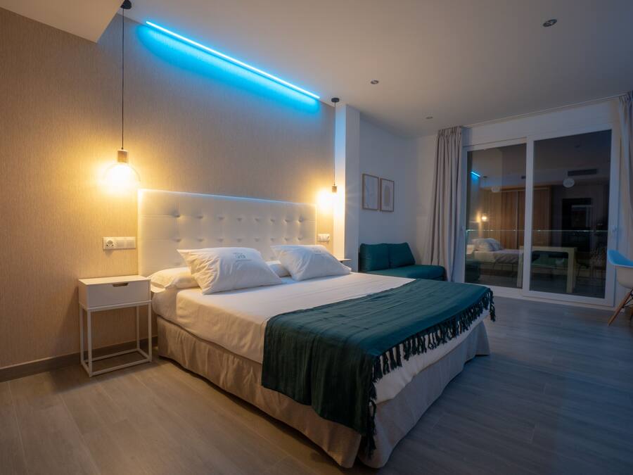 Una habitación de hotel moderna con una cama grande, una mesita de noche, una manta verde y vistas al exterior a través de una puerta corrediza de vidrio.