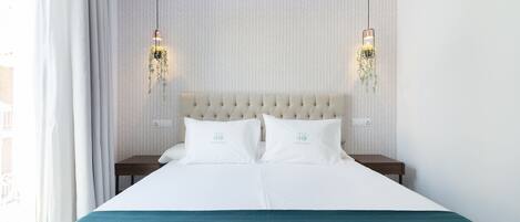 Een netjes opgemaakt bed met een blauwgroene sprei, twee witte kussens en een gestuikt hoofdbord. Er staan twee nachtkastjes met lampen, en de muur heeft een visgraatmotief.