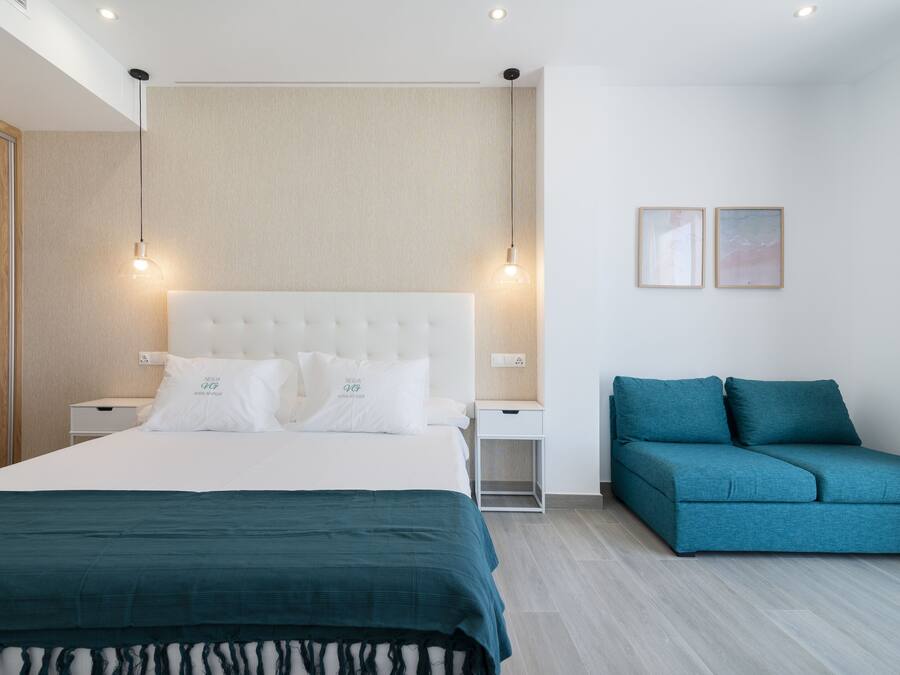 A modern bedroom with a large bed, a nightstand, a blue sofa, and two wall-mounted lights.