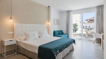 Quarto de hotel moderno com uma cama grande, uma mesa de cabeceira, uma cadeira e vista para o exterior.
