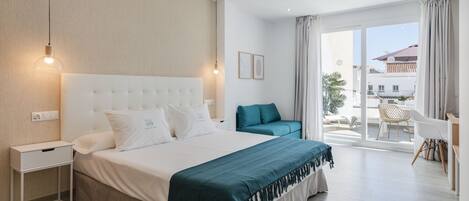 Una habitación de hotel moderna con una cama grande, una mesita de noche, una silla y vistas al exterior.