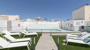 Un área de piscina en la azotea con sillones blancos y una vista despejada del horizonte de la ciudad.
