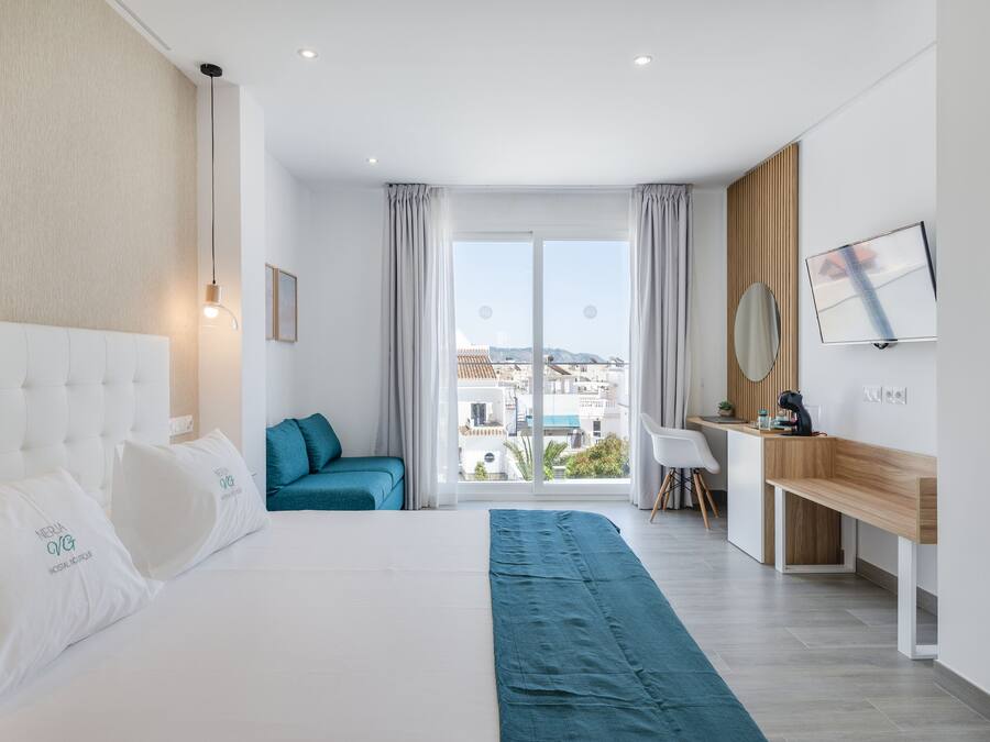 A modern hotel room with a large bed, a desk, and a view of the city through the window.