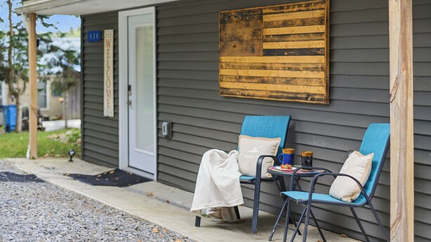 A porch with two blue chairs, a welcome sign, and a wooden artwork on the wall. - Lakefront, 5 Min to Colgate, Sleeps 8 (Hamilton)