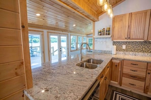 Cocina con alacenas de madera, encimeras de granito, pileta de acero inoxidable y vista al exterior.