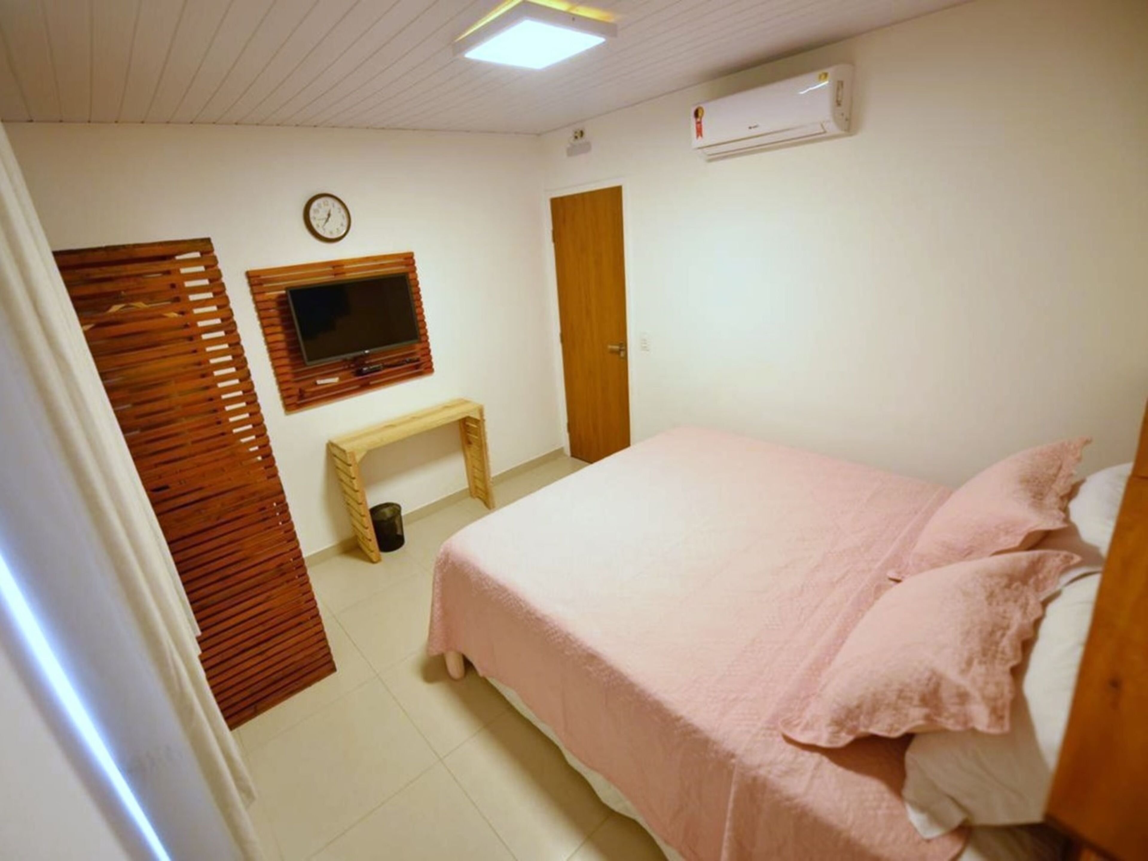 A bedroom with a bed, a TV, a wooden bench, and a door.