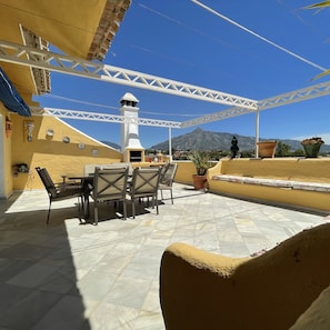 An outdoor patio with a table and chairs, a white pergola, and a view of mountains.