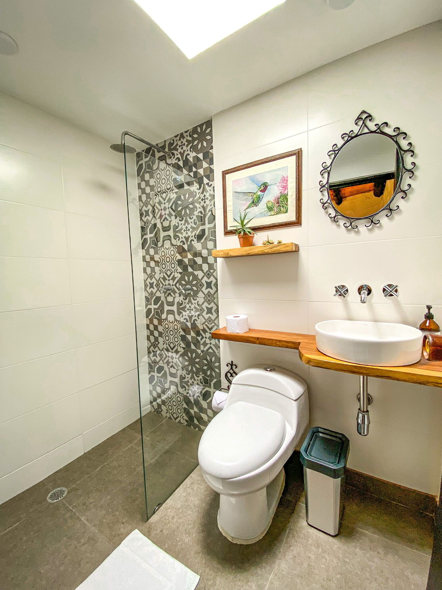 A bathroom with a toilet, sink, and shower. There is a patterned wall and a mirror above the sink.