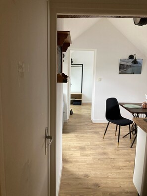 Un pasillo que conduce a un comedor con una mesa y sillas, piso de madera y un cuadro en la pared.