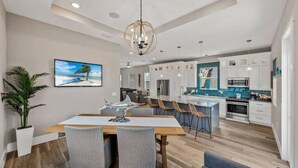 A modern kitchen with white cabinets, a central island, and a dining area with a wooden table and chairs. - Luxury Coastal Home, Gulfport Waterfront District (Gulfport)