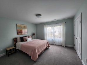 Une chambre à coucher avec un lit, une table de chevet, une lampe, un tableau et une fenêtre avec des rideaux.