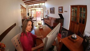 A person using a desktop computer in a room with a wooden table, a sofa, and a door with glass panels. - Hotel Puerto de Vega (Vallenar)