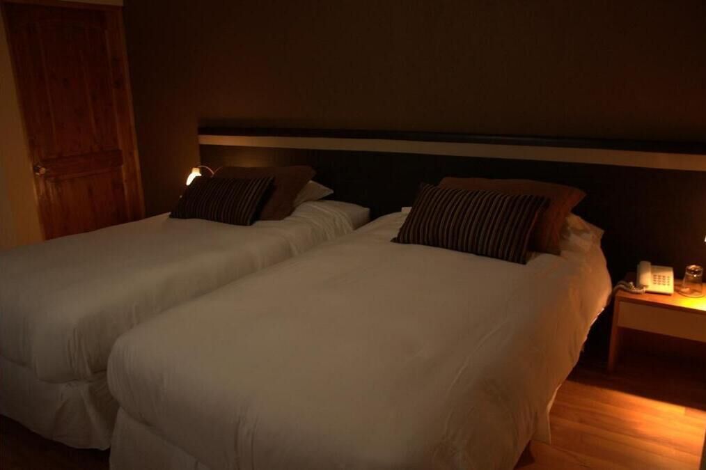 Habitación de hotel con dos camas, una puerta de madera, una mesita de noche con lámpara y un teléfono.