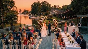 A wedding ceremony on a wooden deck with a view of a lake and houses in the background.