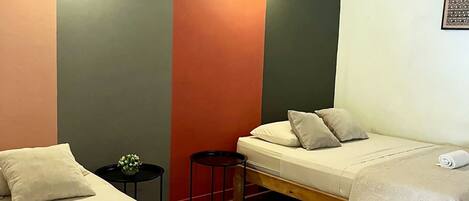 A room with two beds, a small table, and a wall-mounted light fixture.