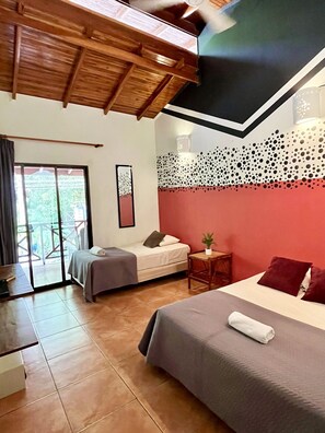 A hotel room with two beds, a small table, a chair, a balcony, and a wooden ceiling.