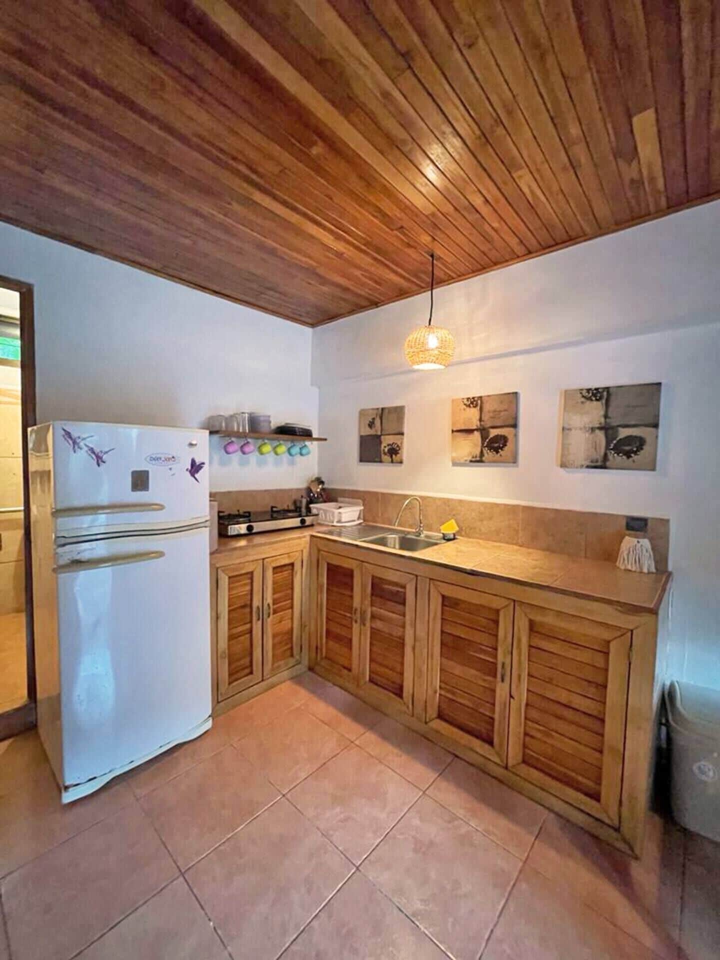 A kitchen with wooden cabinets, a white refrigerator, and a hanging light fixture.