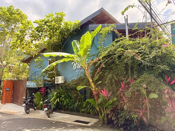 A building with a reception area, a motorcycle parked outside, and lush greenery around.