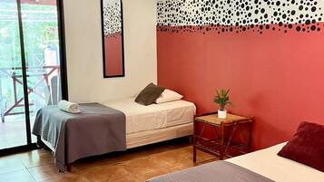 Ein Hotelzimmer mit zwei Betten, einer roten Akzentwand, einem Deckenventilator und einer Glasschiebetür zu einem Außenbereich.
