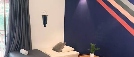 A room with two beds, a small table with a plant, and a wall with a colorful stripe design.
