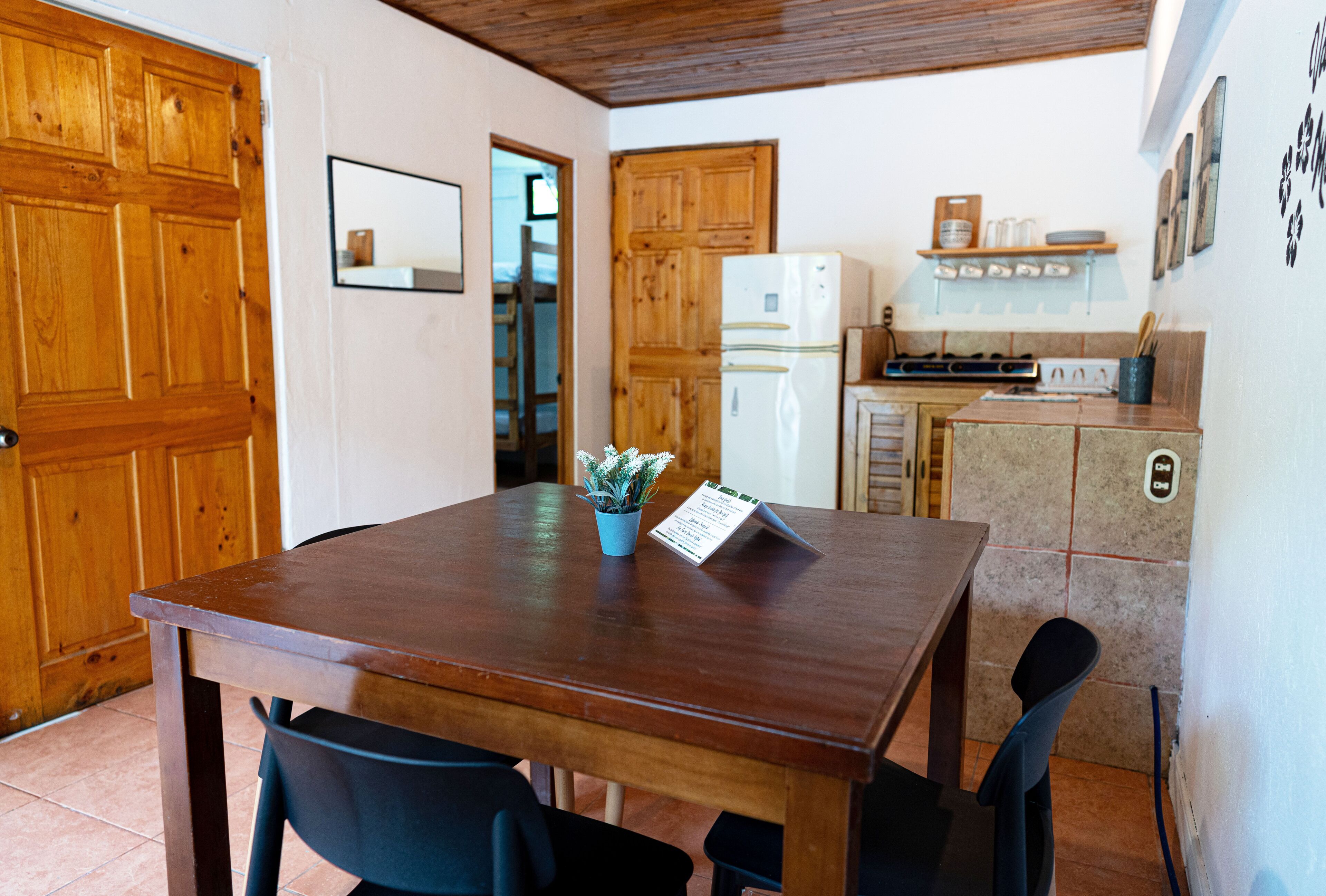 Una mesa de madera para comer con sillas, una pequeña planta en maceta y un atril para el menú.