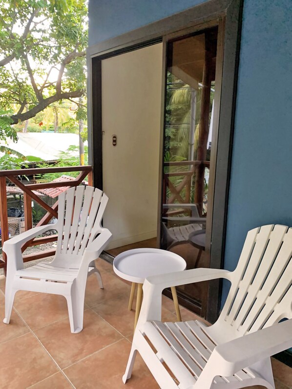 Een balkon met witte plastic stoelen, een ronde tafeltje, een schuifdeur en uitzicht op groen.